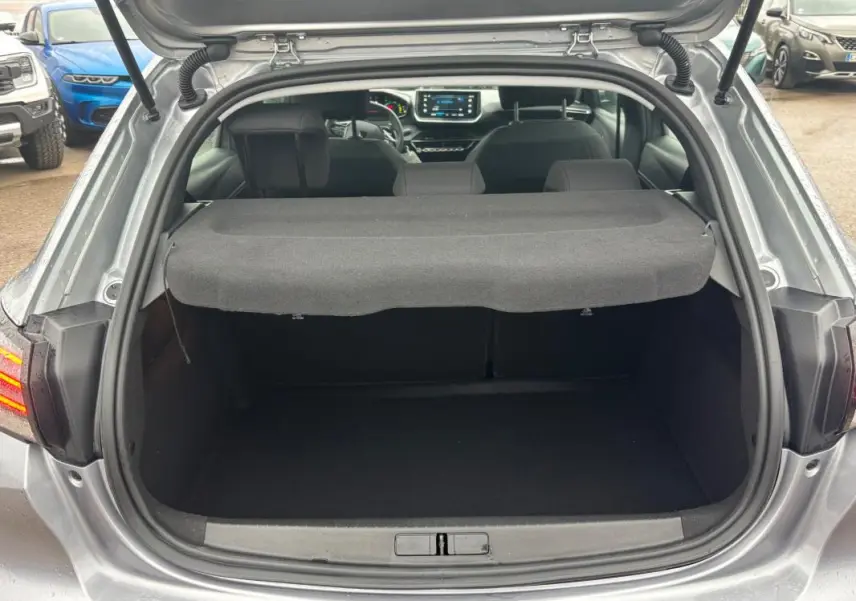 Coffre ouvert vu de l'arrière d'une Peugeot 208 gris 2025, avec tablette cache-bagages et intérieur visible.