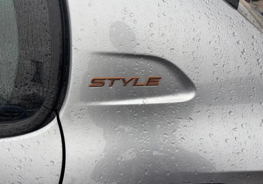 Gros plan sur l’inscription Style en orange sur la portière gris clair mouillée d’une Peugeot 208 Hybrid 2025.
