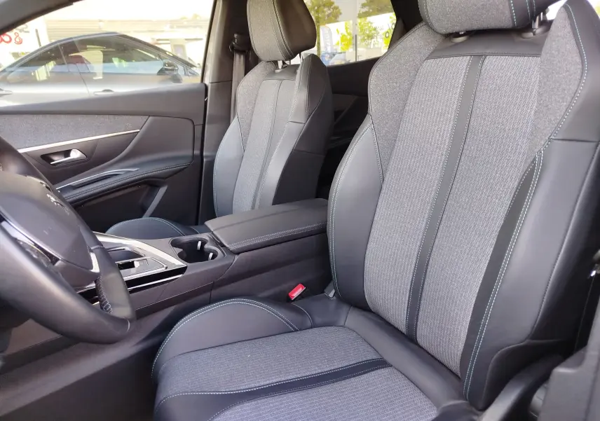 Vue intérieure côté conducteur du Peugeot 3008 2023, sièges tissu et cuir gris avec surpiqûres bleues.