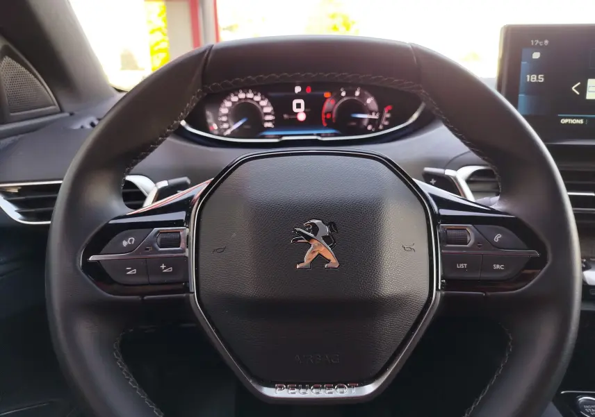 Gros plan sur le volant multifonction noir du Peugeot 3008 2023 avec tableau de bord numérique en arrière-plan.