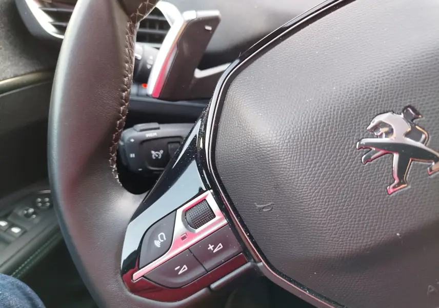 Gros plan sur le volant cuir noir du Peugeot 3008 2023 avec commandes intégrées et logo lion chromé.