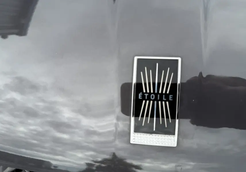 Gros plan sur l'écusson ÉTOILE noir et argent sur la carrosserie gris foncé du DS3 hybride 2025.