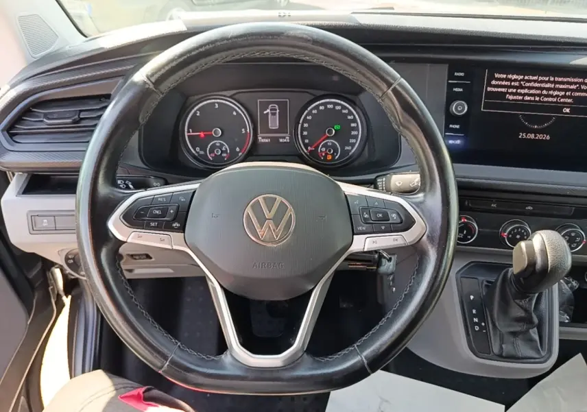 Vue intérieure centrée sur le volant cuir multifonctions et tableau de bord numérique du Volkswagen Transporter gris foncé.