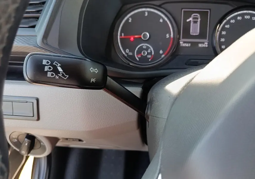Gros plan intérieur sur le tableau de bord et levier de clignotant du Volkswagen Transporter gris foncé, affichage des compteurs visible.