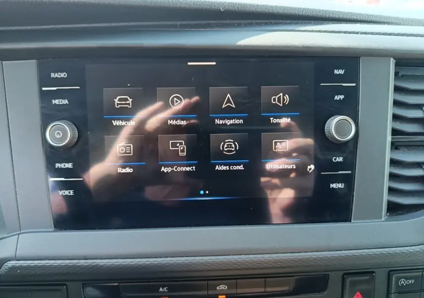 Écran tactile central du Volkswagen Transporter 2022 affichant les menus navigation et médias, avec reflets de mains.