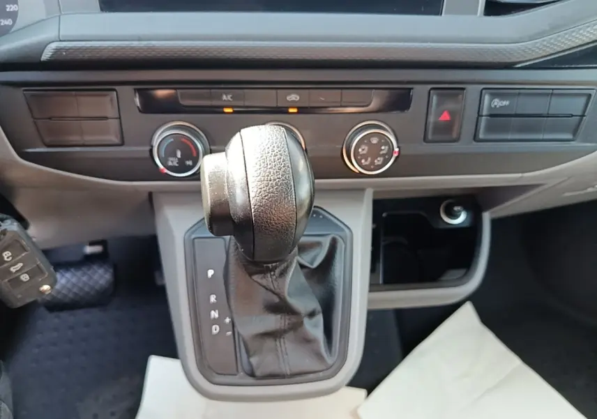 Gros plan sur le levier de vitesses automatique en cuir noir du Volkswagen Transporter gris foncé, tableau de bord en arrière-plan.