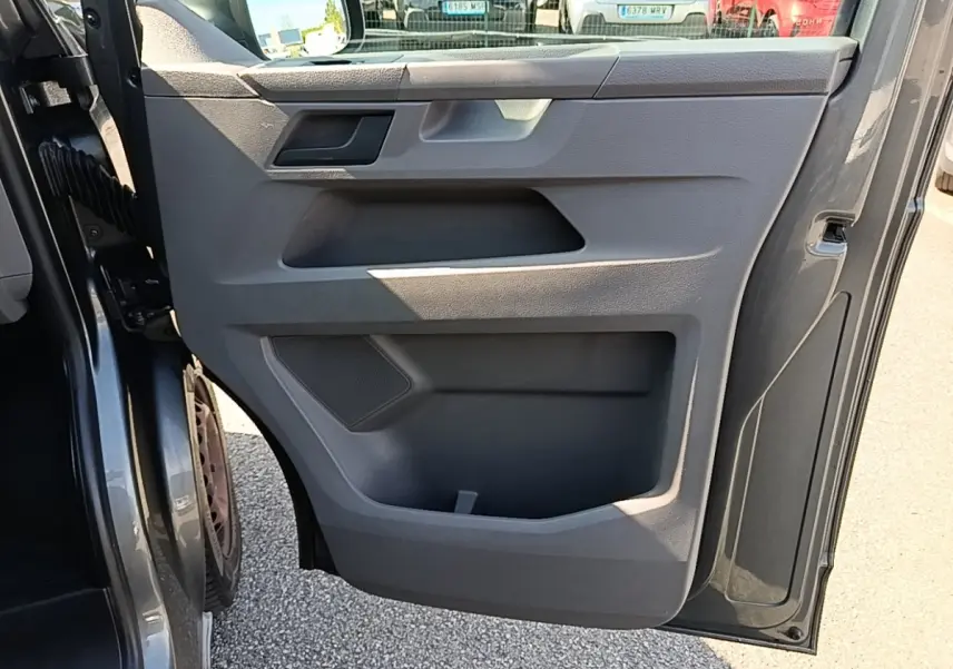 Vue rapprochée de la porte avant gauche ouverte d’un Volkswagen Transporter gris foncé, montrant le panneau intérieur en plastique gris.