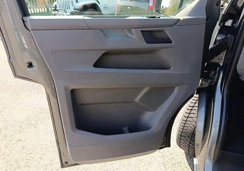 Vue rapprochée de la porte arrière droite ouverte d’un Volkswagen Transporter gris foncé, montrant le panneau intérieur en plastique gris.