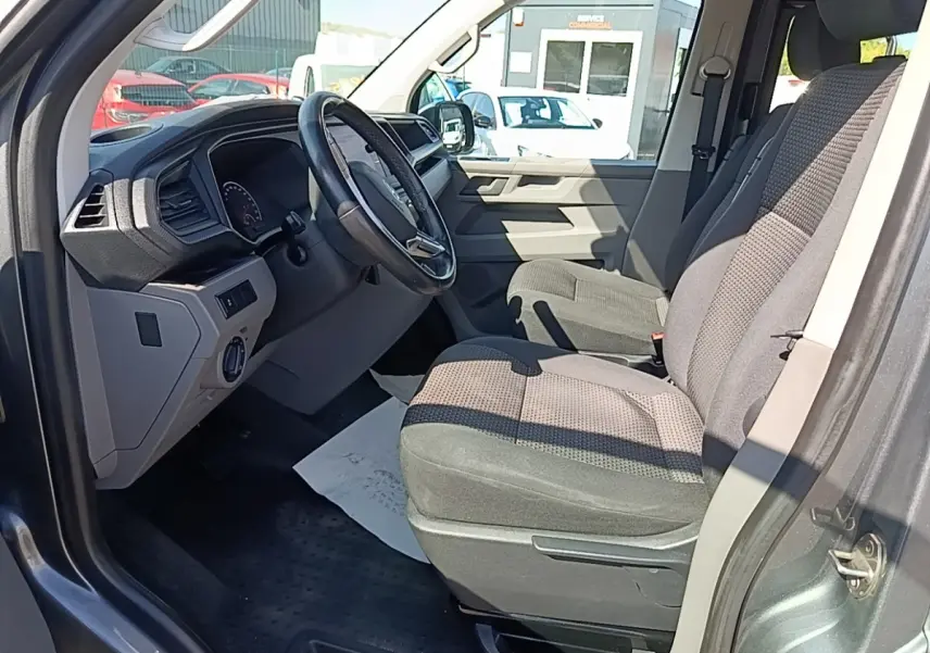 Vue intérieure côté conducteur du Volkswagen Transporter gris foncé, montrant le volant cuir multifonctions et les sièges tissu.