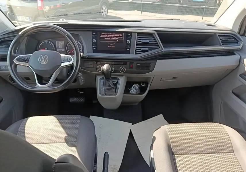 Vue intérieure avant du Volkswagen Transporter 2.0 TDi gris, tableau de bord avec écran tactile et volant multifonctions cuir.