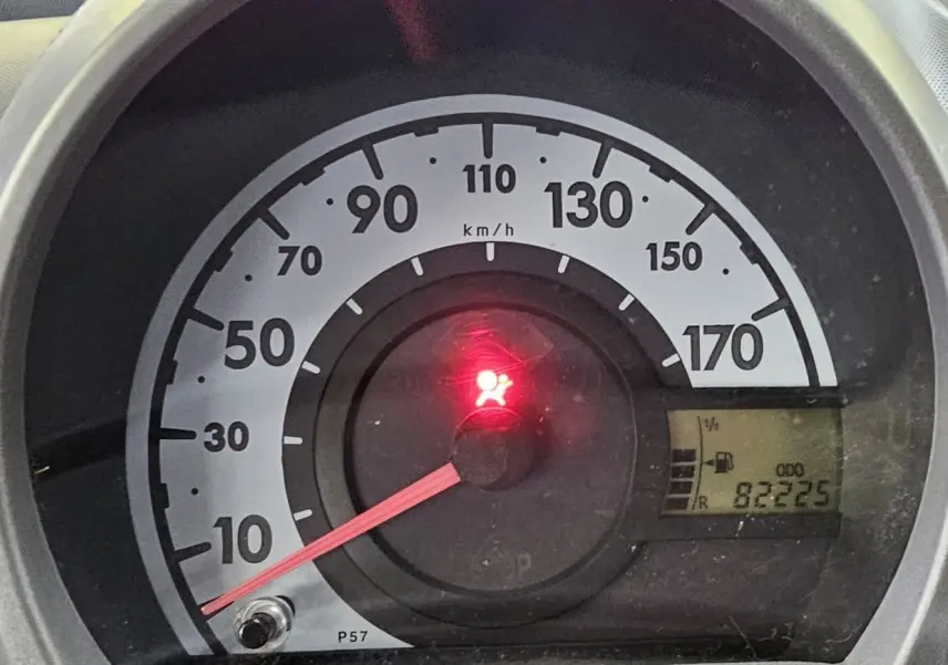 Gros plan sur le compteur de vitesse d'une Peugeot 107 jaune, affichant 82 225 km et voyant airbag allumé.