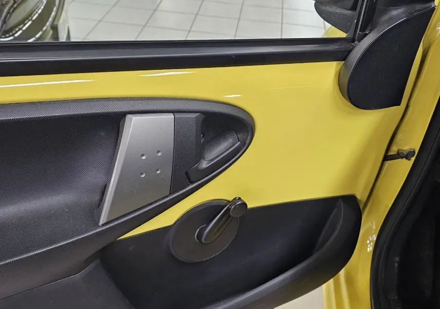 Intérieur de la porte avant gauche jaune d'une Peugeot 107 2013, avec poignée manuelle de vitre et panneau noir texturé.