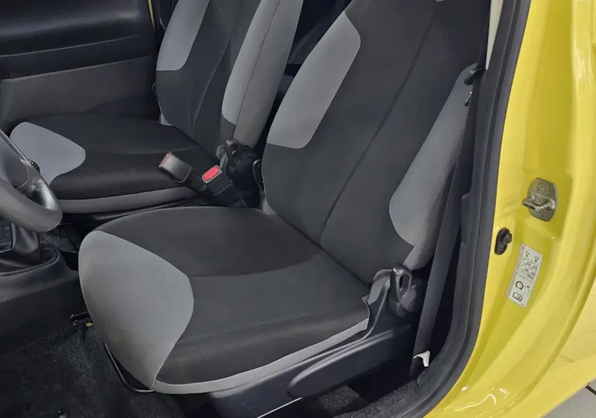 Intérieur côté conducteur d'une Peugeot 107 jaune 2013, sièges tissu noir et gris, volant et levier de vitesses visibles.
