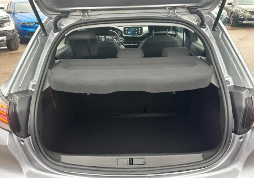Coffre ouvert d'une Peugeot 208 gris 3/4 arrière, avec tablette cache-bagages et intérieur visible jusqu'au tableau de bord.