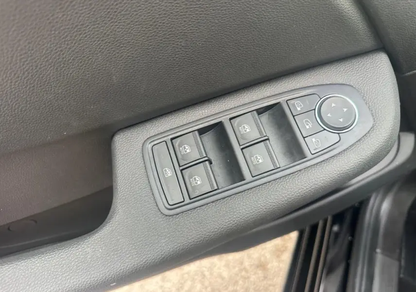 Gros plan sur les commandes des vitres électriques et des rétroviseurs sur la porte côté conducteur d’une Renault Clio noire.