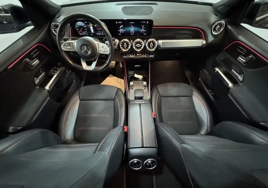 Vue intérieure avant du Mercedes GLB 200 d AMG Line noir, avec tableau de bord numérique et éclairage d'ambiance rouge.
