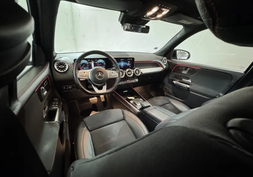 Vue intérieure avant du Mercedes GLB 200 d AMG Line noir, tableau de bord digital et éclairage d'ambiance rouge.