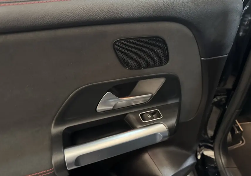 Détail de la porte intérieure côté gauche du Mercedes GLB 200 d AMG Line noir, avec poignée argentée et commande de fenêtre.