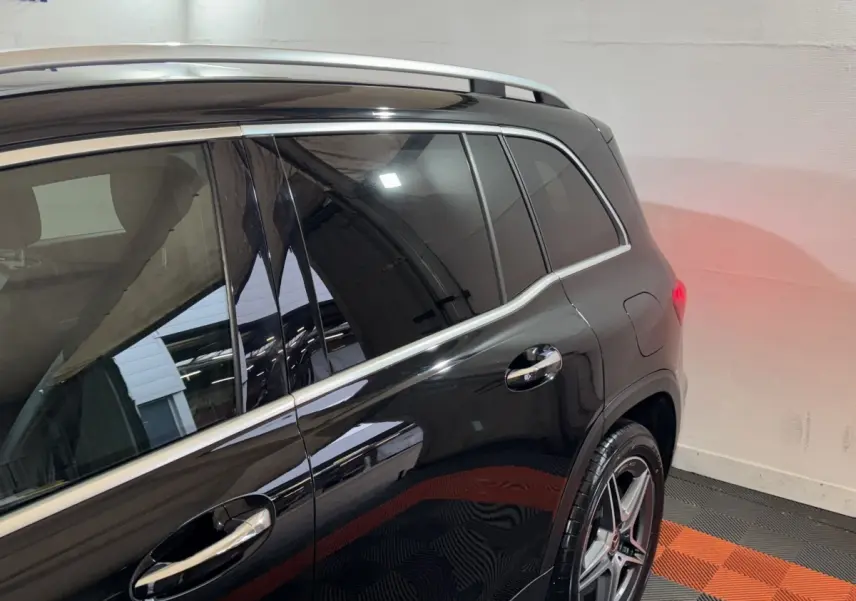Vue latérale arrière droite d’un Mercedes GLB 200 d AMG Line noir avec jantes alliage et barres de toit chromées.