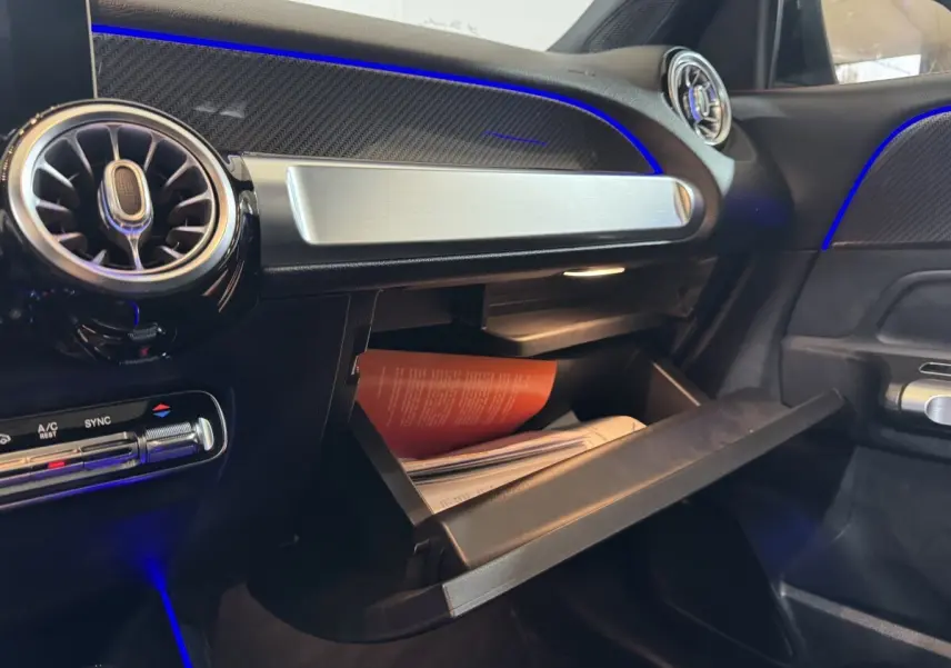 Intérieur du Mercedes GLB 200 d AMG Line noir, vue côté passager sur boîte à gants ouverte avec éclairage bleu d'ambiance.