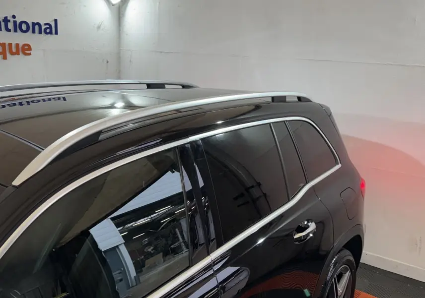 Vue 3/4 arrière droite du Mercedes GLB 200 d AMG Line noir avec barres de toit chromées et vitres teintées.