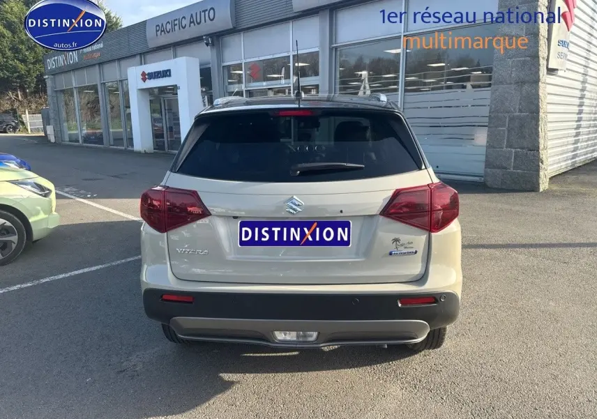 Vue arrière d'un Suzuki Vitara 1.4 Boosterjet Hybrid 2026 en So'Color Savanna Ivory/Black métal, avec feux arrière LED et barres de toit visibles.