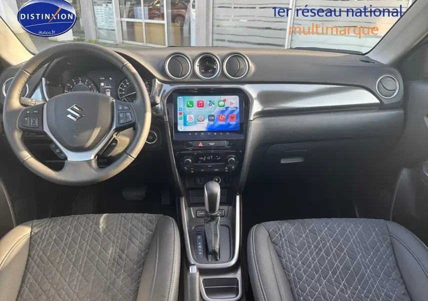 Vue intérieure avant du Suzuki Vitara 1.4 Boosterjet Hybrid 2026, volant multifonction, écran tactile et sièges en suédine noire.