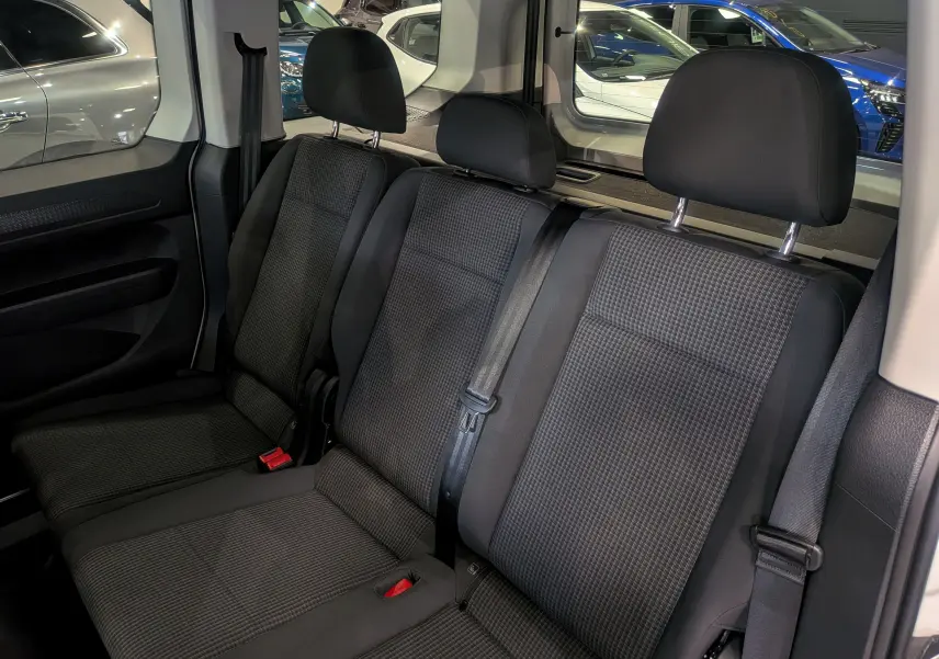 Vue intérieure des sièges arrière en tissu noir du Volkswagen Caddy 2.0 TDI 2025, avec ceintures de sécurité visibles.