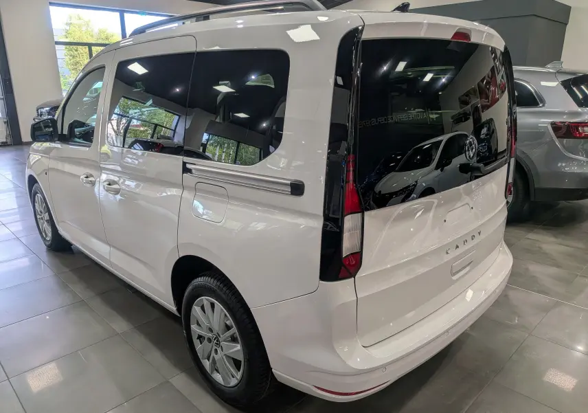 Vue 3/4 arrière droite d’un Volkswagen Caddy blanc 2025 avec vitres arrière teintées et jantes alliage en showroom.