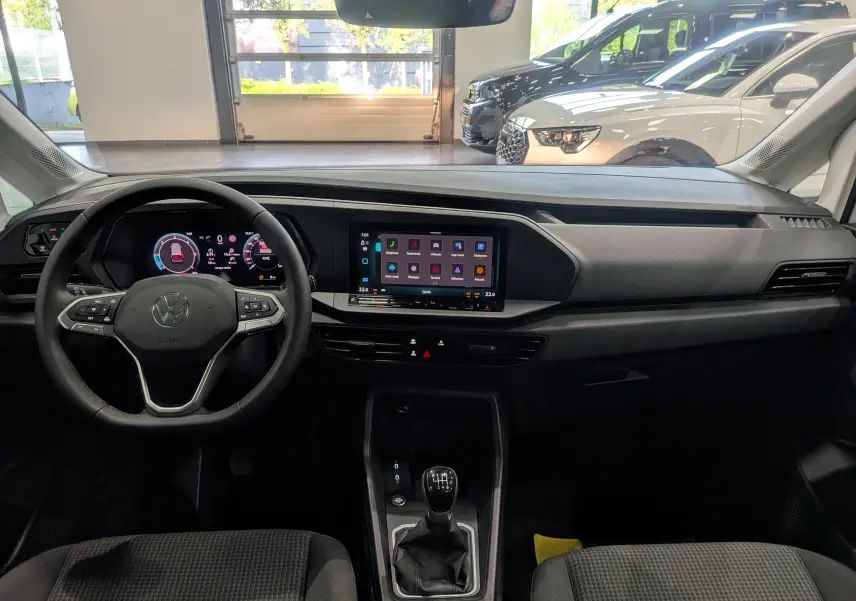 Vue intérieure avant du Volkswagen Caddy blanc 2025, avec tableau de bord numérique et écran tactile central.