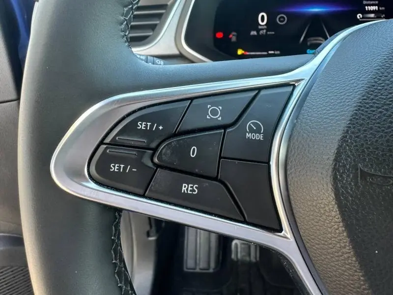 Gros plan sur les commandes au volant côté gauche du Renault Captur 2025 Bleu Iron/Noir Étoilé avec affichage numérique en arrière-plan.