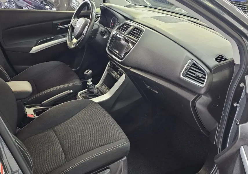 Intérieur avant du Suzuki SX4 S-Cross gris 2020, vue côté conducteur montrant sièges noirs et tableau de bord moderne.