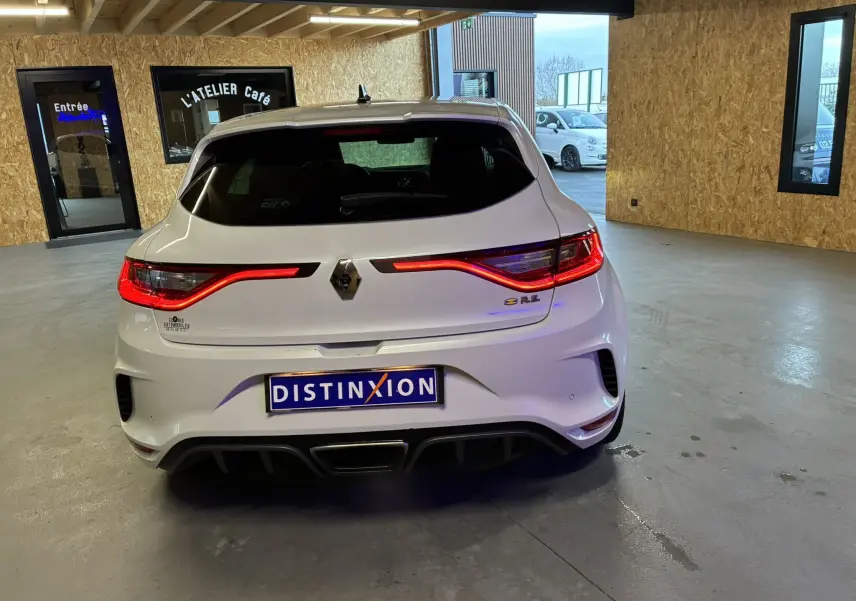 Vue arrière d'une Renault Mégane IV RS 280 EDC6 blanche avec feux LED allumés dans un garage.