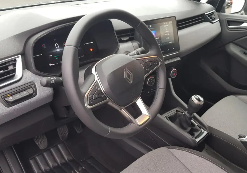 Vue intérieure côté conducteur de la Renault Clio gris 2025 avec volant multifonction et boîte manuelle.