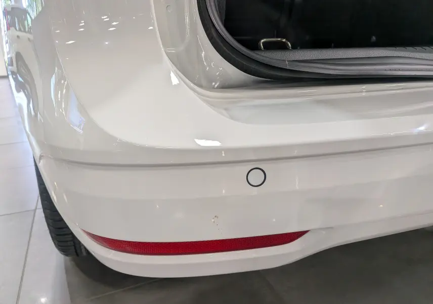 Gros plan sur le pare-chocs arrière blanc du Volkswagen Caddy 2025 avec capteur de recul et feu rouge intégré.