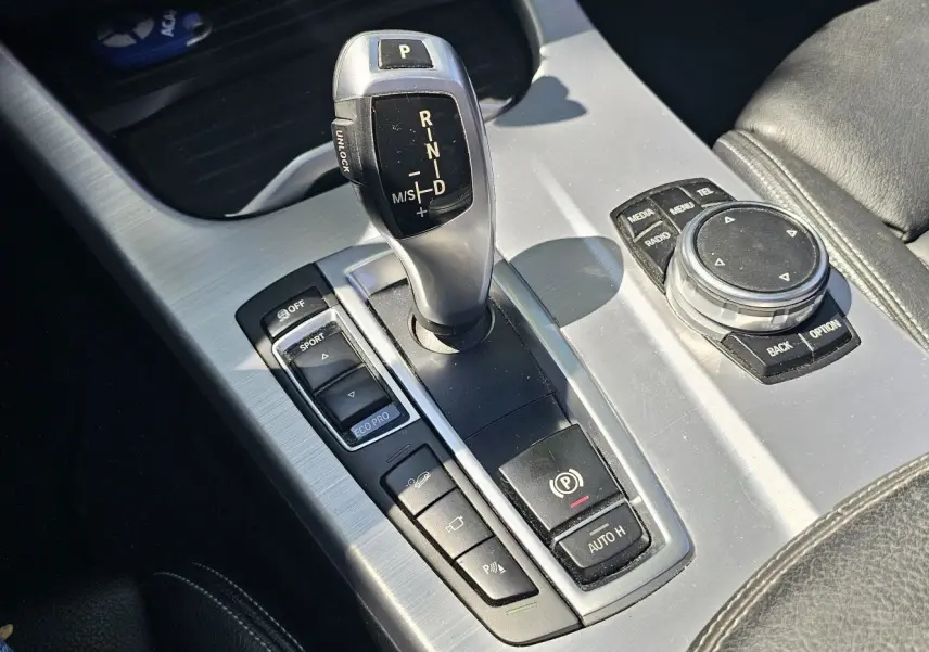 Gros plan sur la console centrale argentée du BMW X4 xDrive20d noir, avec levier de vitesse et commandes multimédia.