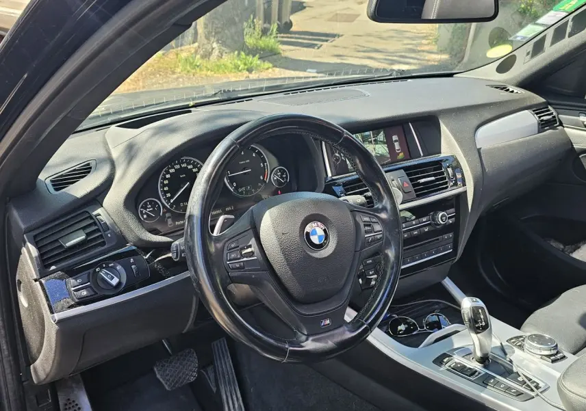 Vue intérieure côté conducteur d'un BMW X4 xDrive20dA noir, avec volant multifonction et tableau de bord moderne.