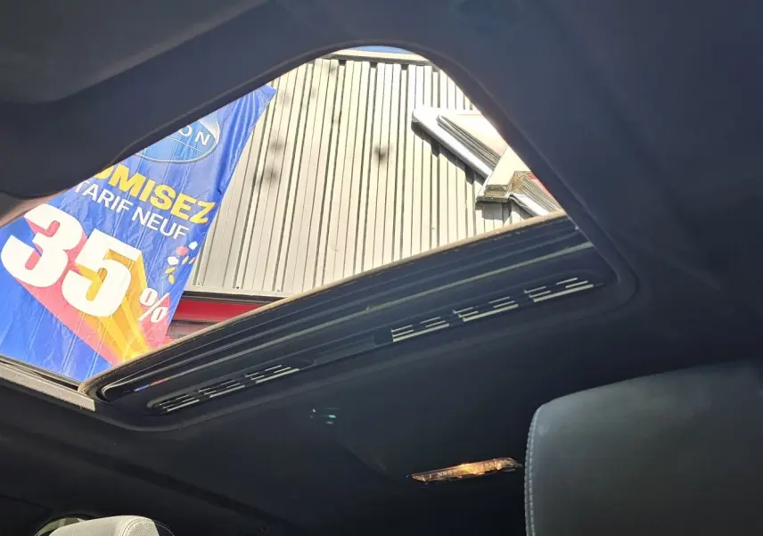 Toit ouvrant panoramique ouvert vu de l'intérieur d'une BMW X4 xDrive20dA noire, avec ciel et bannière publicitaire en arrière-plan.