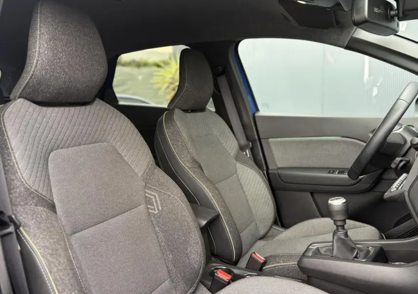 Vue intérieure côté droit du Renault Captur 2025, sièges tissu gris avec surpiqûres jaunes et levier de vitesse manuel.