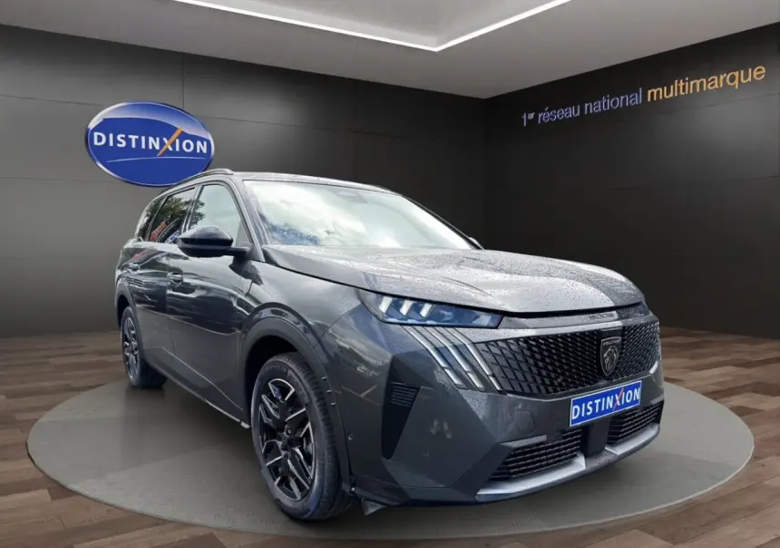 Peugeot 5008 gris foncé en 3/4 avant droit, avec calandre distinctive et jantes noires brillantes.