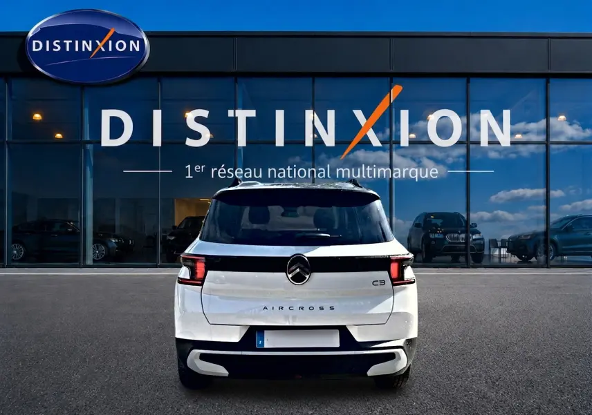 Vue arrière d'un Citroën C3 Aircross blanc garé devant une vitrine avec logo Distinxion visible.