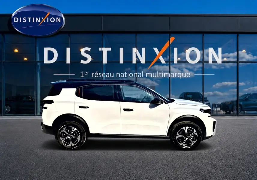 Profil droit d’un Citroën C3 Aircross blanc 2026 avec toit noir et jantes alu devant une vitrine Distinxion.