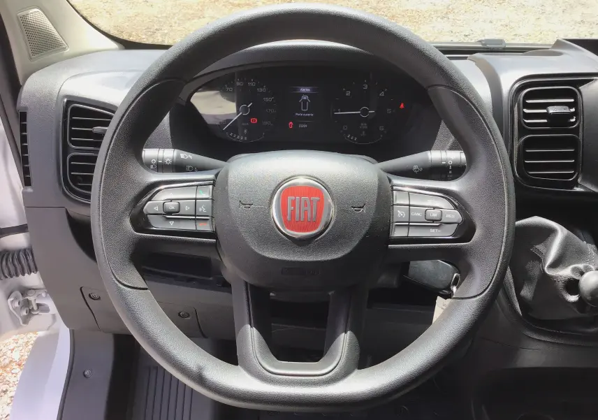 Vue rapprochée du volant noir FIAT avec commandes intégrées et tableau de bord numérique du Ducato Fourgon blanc 2024.