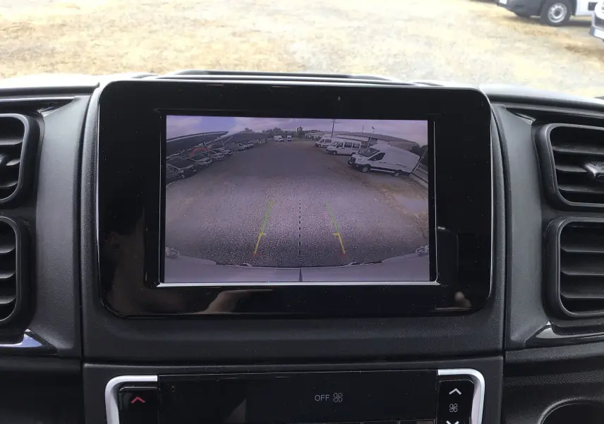 Écran de caméra de recul montrant un parking avec plusieurs fourgons blancs, depuis l’intérieur d’un Fiat Ducato blanc.