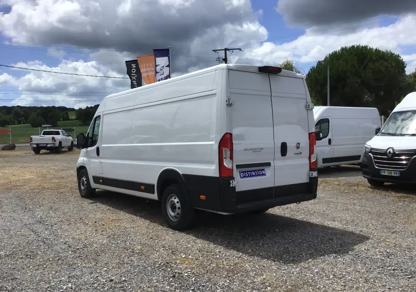 Fiat Ducato Fourgon blanc vu en 3/4 arrière droit sur un parking extérieur avec ciel nuageux.