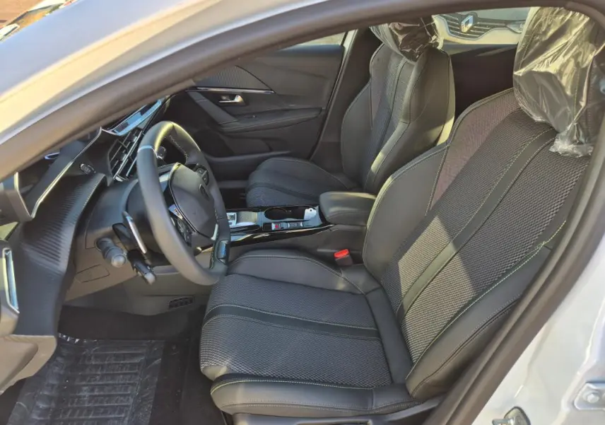 Vue intérieure côté conducteur de la Peugeot 208 Hybrid 136 GT blanche, avec sièges en tissu et volant multifonction.