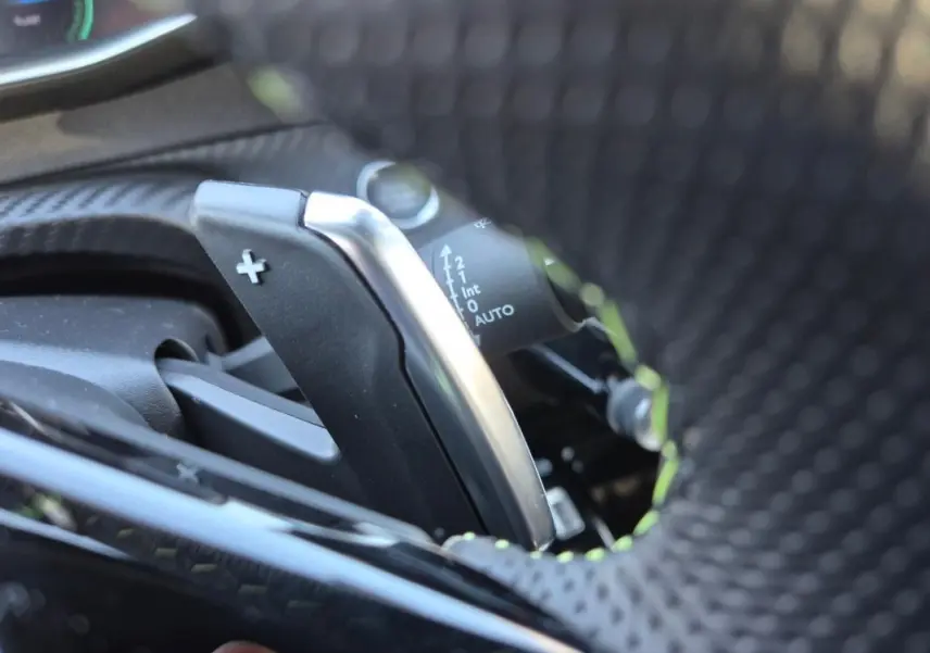 Gros plan sur la palette de changement de vitesse + du volant perforé d'une Peugeot 208 Hybrid 136 e-DCS6 GT blanc.