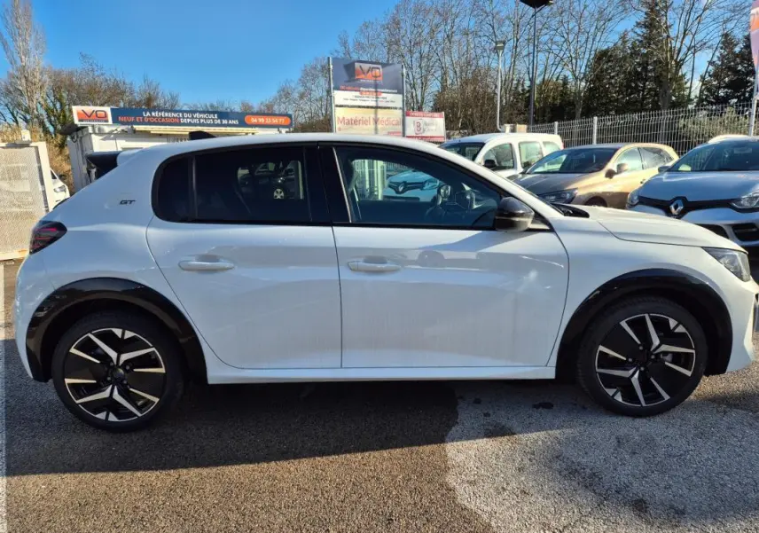 Profil droit d’une Peugeot 208 Hybrid 136 e-DCS6 GT blanche avec jantes alliage 17 pouces et logo GT sur l’aile arrière.