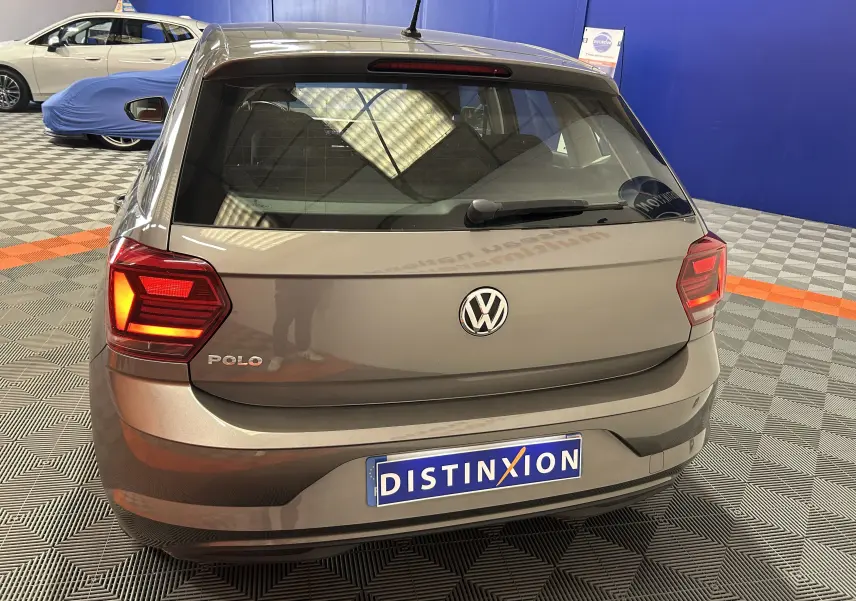 Vue arrière d'une Volkswagen Polo gris métallisé avec feux allumés, stationnée en intérieur sur sol damier.