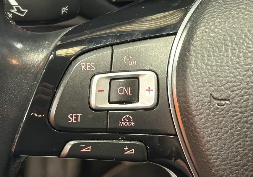 Gros plan sur les commandes de régulateur de vitesse à gauche du volant en cuir noir d’une Volkswagen Polo gris 2018.